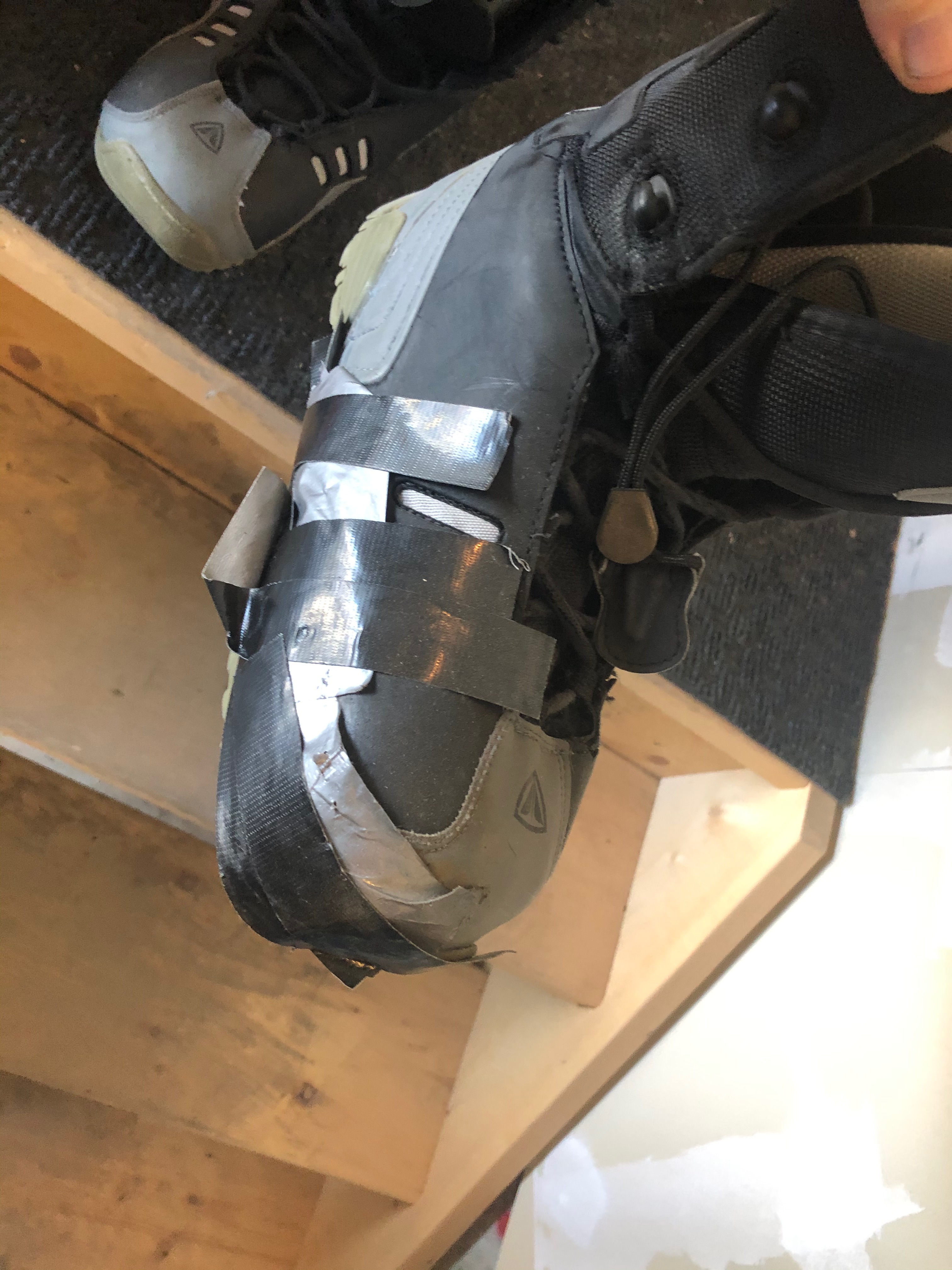 A close-up of duct tape repairing a seam on old snowboard boots.