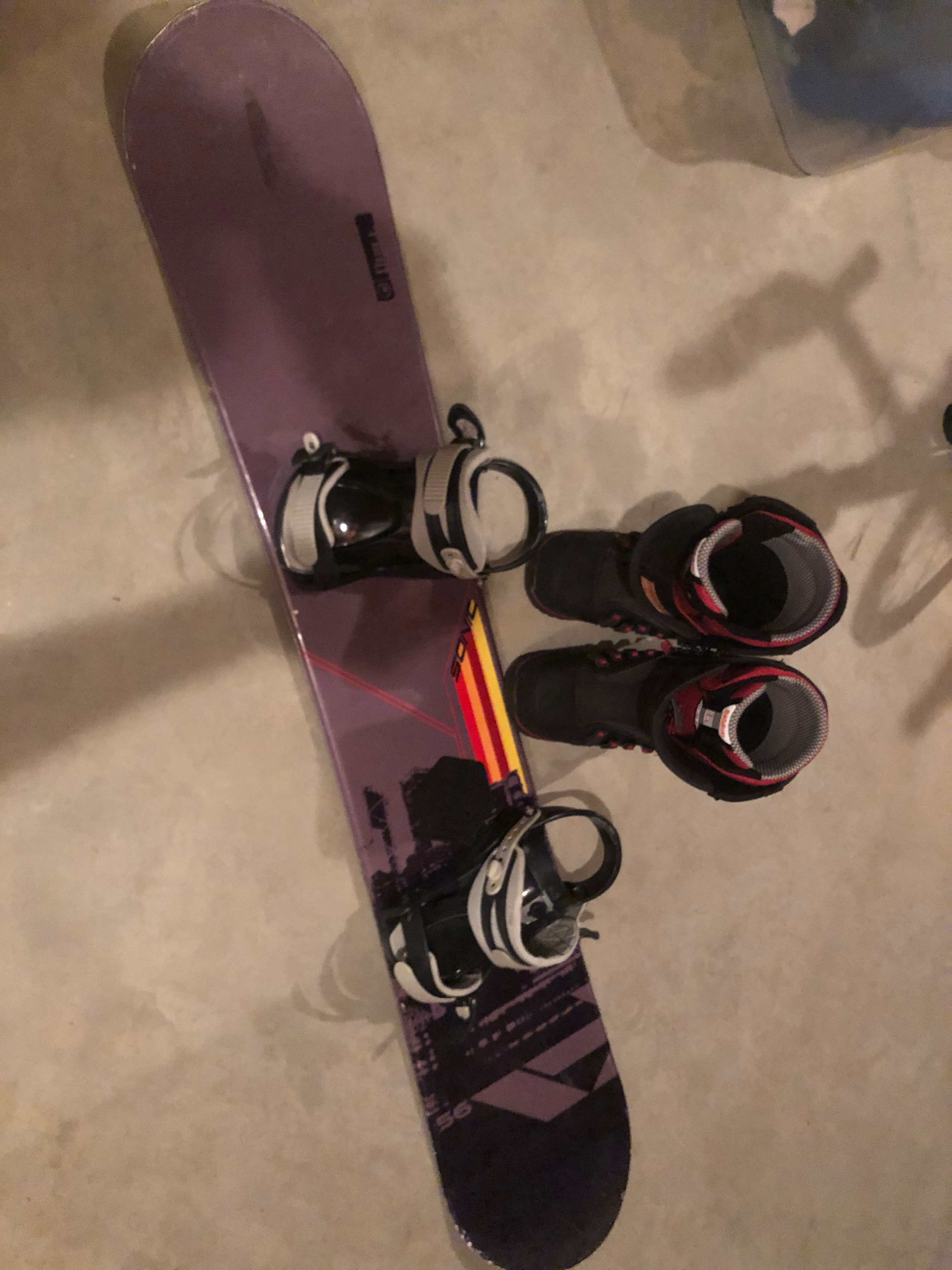 An old snowboard with bindings and a smaller pair of boots.